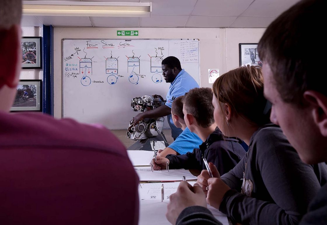 An image of young people with a teacher showing them an engine as part in the Archway project, a motorcycle education and youth centre programme supported by the Ellis Campbell Foundation, helping disadvantaged young people in Hampshire, London and Perthshire