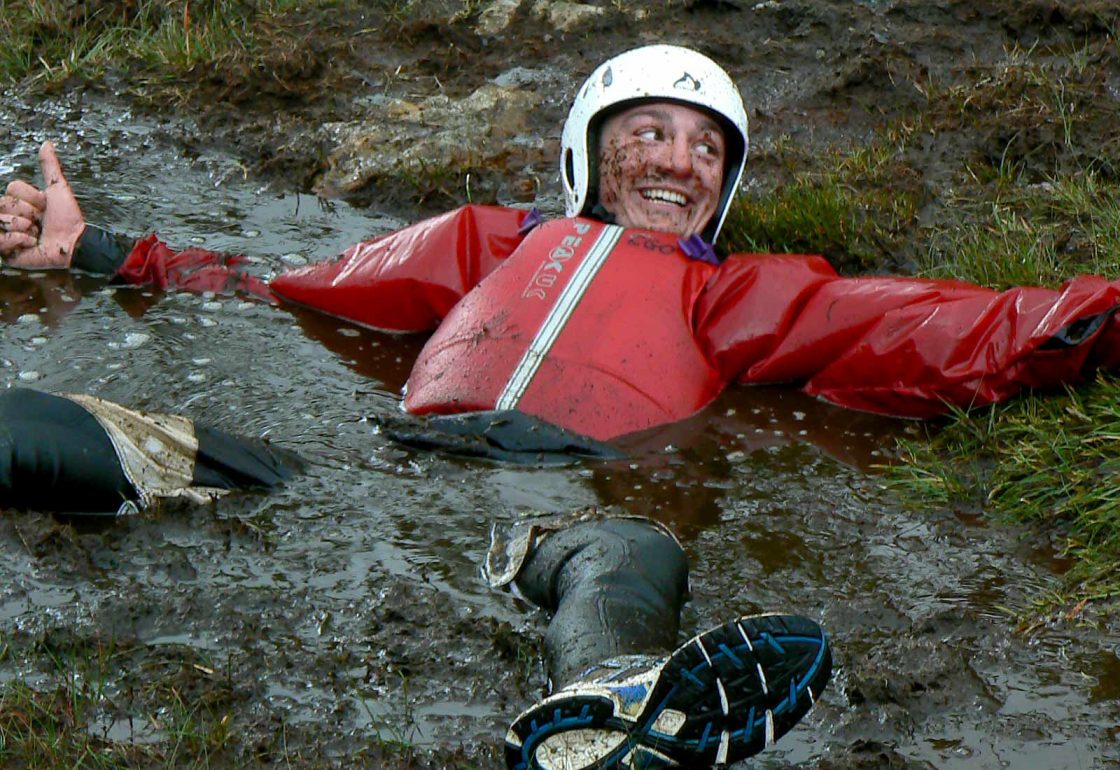 An image of a guy lying in mud and water taking part a Climbing Out activity , a charity supported by the Ellis Campbell Foundation, helping disadvantaged young people in Hampshire, London and Perthshire