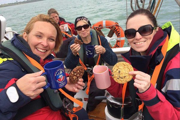 An image of a group of young women eating biscuits and drinking tea aboard a boat, participating in Ocean Youth Trust South, a charity supported by the Ellis Campbell Foundation, helping disadvantaged young people in Hampshire, London and Perthshire
