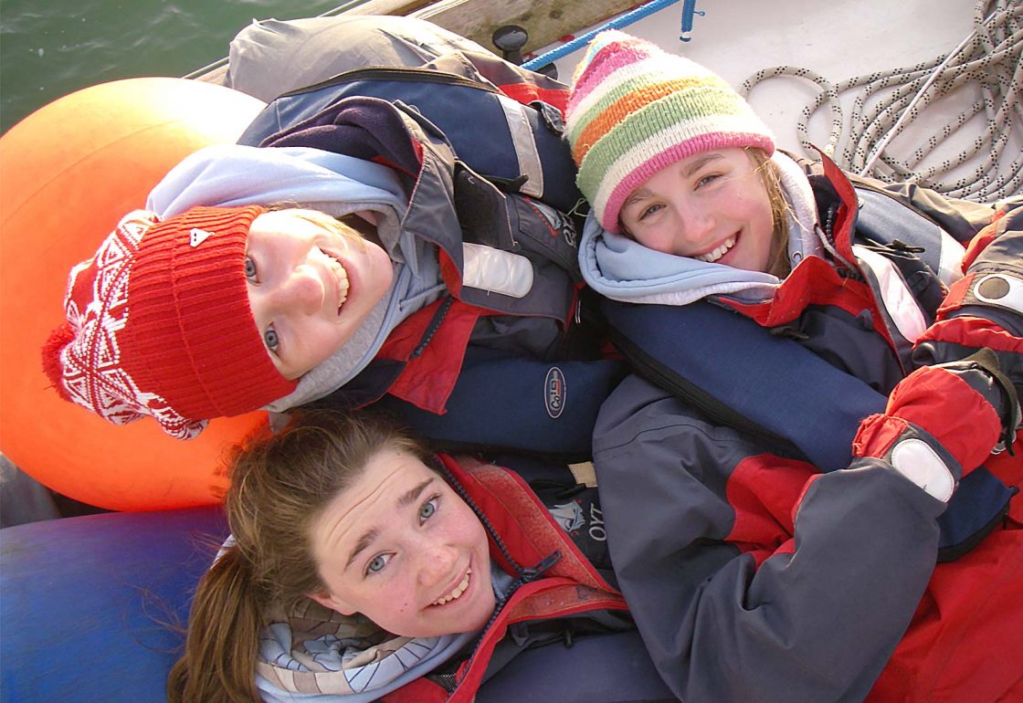 An image of three young people smiling aboard a sailing boat part of Ocean Youth Trust South, a charity supported by the Ellis Campbell Foundation, helping disadvantaged young people in Hampshire, London and Perthshire