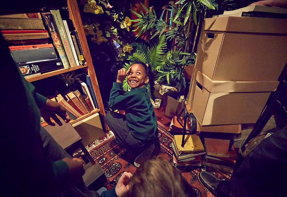 An image of a smiling child amongst props used by Punchdrunk theatrical experiences, a charity supported by the Ellis Campbell Foundation, helping disadvantaged young people in Hampshire, London and Perthshire