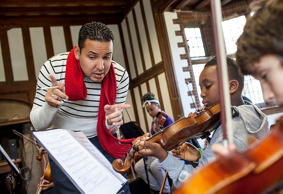 An image of a teacher conducting music with young children playing violins and taking part in Sistema England Social Action Music Programme, a charity supported by the Ellis Campbell Foundation, helping disadvantaged young people in Hampshire, London and Perthshire