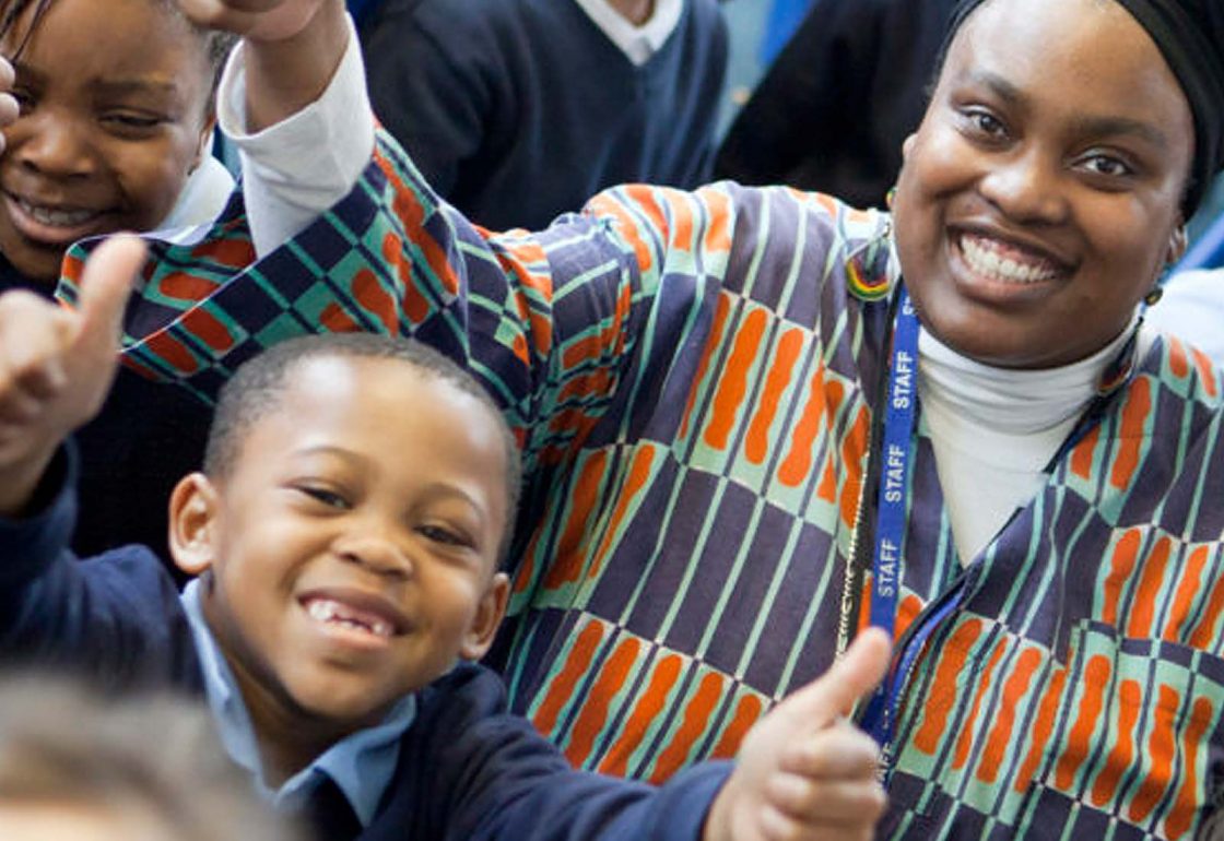 An image of a smiling black teacher with pupils representing the School Home Support Grant made by the Ellis Campbell Foundation helping disadvantaged young people in Hampshire, London and Perthshire