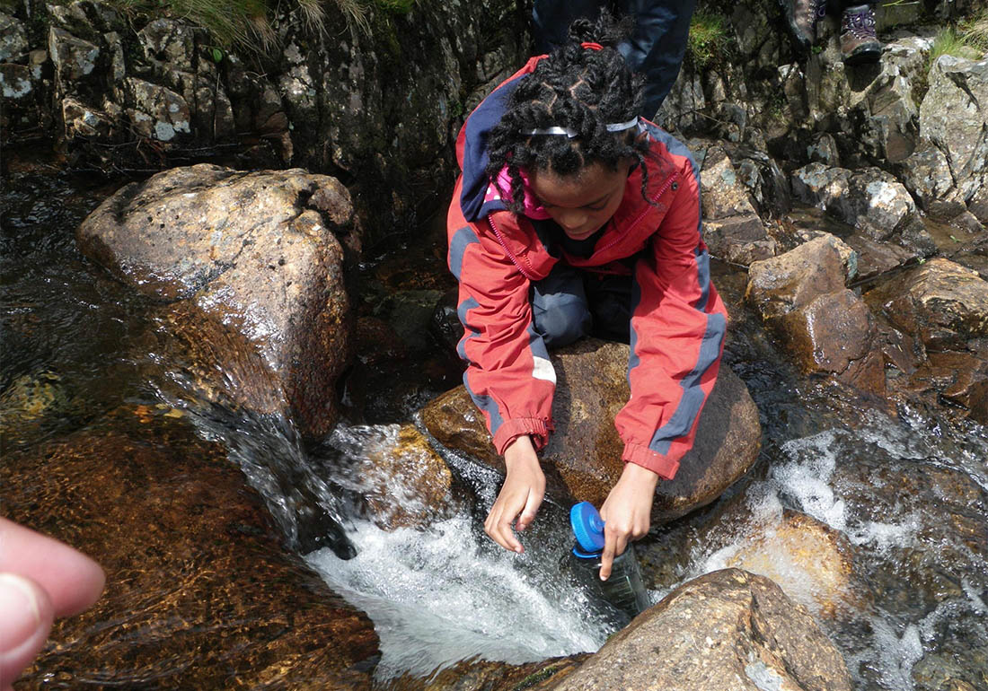 A colour image of a girl taking part in Outward Bound Snowdonia collecting water - A charity supported by The Ellis Campbell Foundation