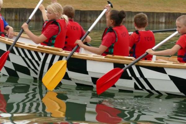 A colour image of a young people sat in a rowing boat on water, wearing red life jackets taking part in the Oarsome Chance programme supported by the Ellis Campbell Foundation