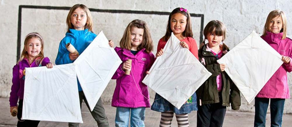 A colour image of six young girls standing in a line holding kites they have made as part of the Remake Scotland Craft Initiative supported by the Ellis Campbell Foundation