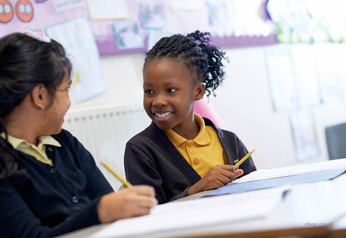 A colour pciture of 2 young girls smiling in a classroom environment as part of the Achievement for All programme supported by The Ellis Campbell Foundation