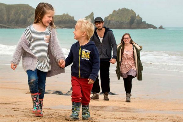 A colour photo fo two children walking along the beach holding hands and smiling - Family Holiday Association grant supported by the Ellis Campbell Foundation