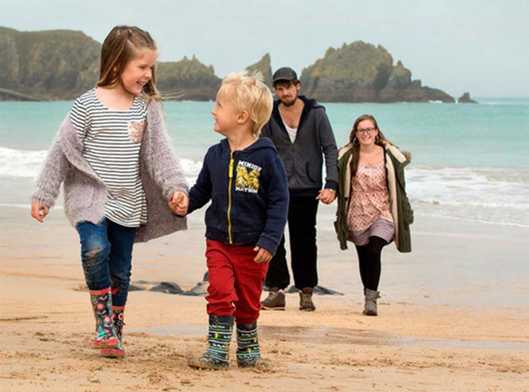 A colour photo fo two children walking along the beach holding hands and smiling - Family Holiday Association grant supported by the Ellis Campbell Foundation